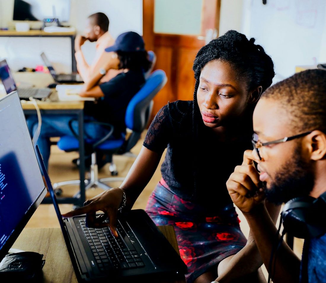 Two colleagues working through something together at a laptop, one pointing at the screen while the other listens.